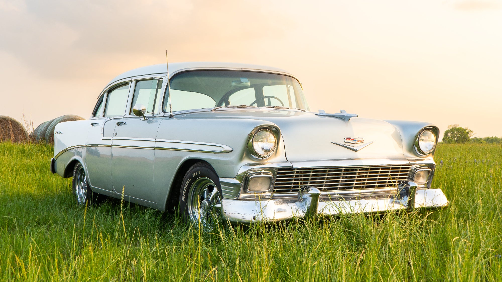 Vintage car in a grassy field with a sunset sky