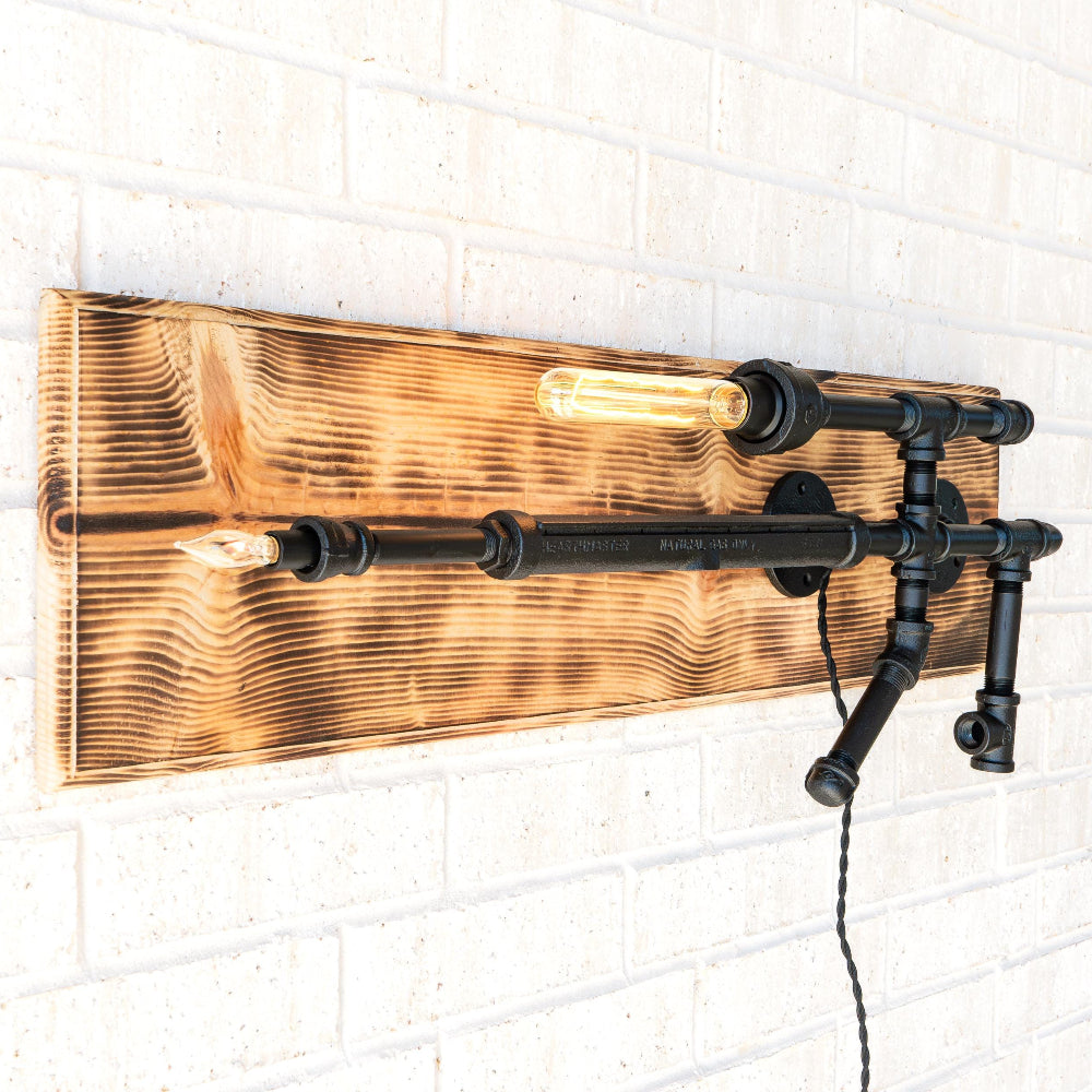 Wall-mounted light fixture with wooden panel and black metal pipes on a white brick wall.