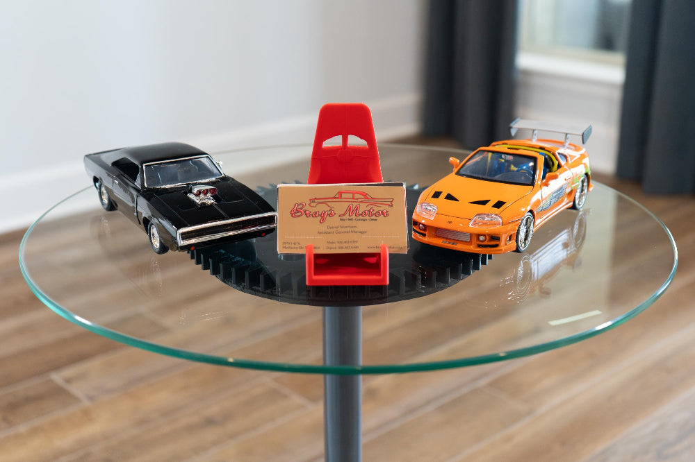 Two toy cars on a glass table with a small sign in the center.