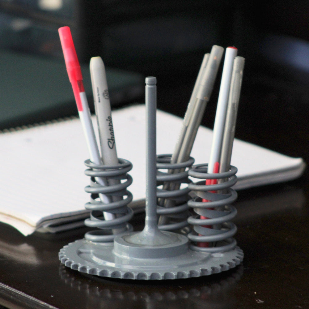 Pens in a unique metal holder on a desk with a notebook in the background