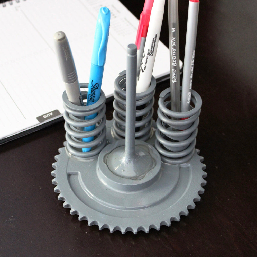 Gray gear-shaped pen holder with pens on a dark surface