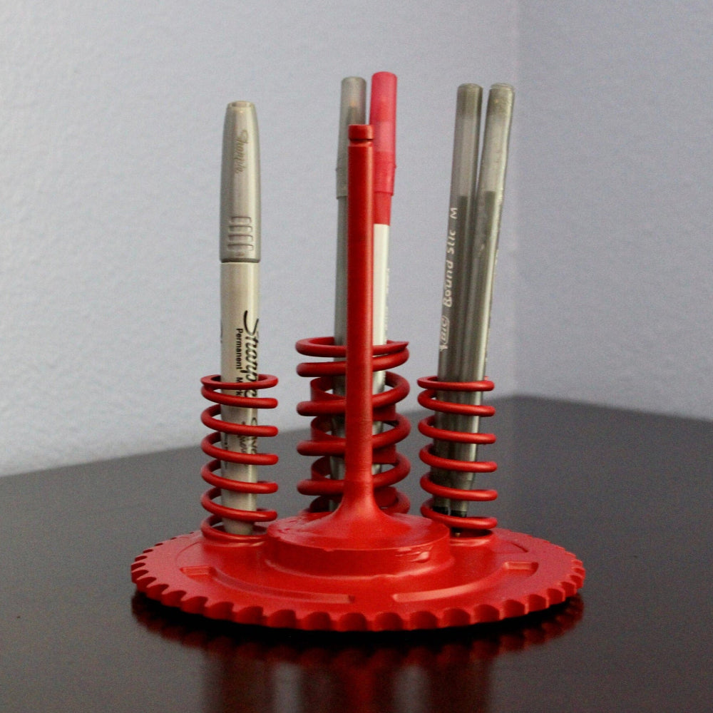 Red pen holder with three pens on a dark surface and light gray background