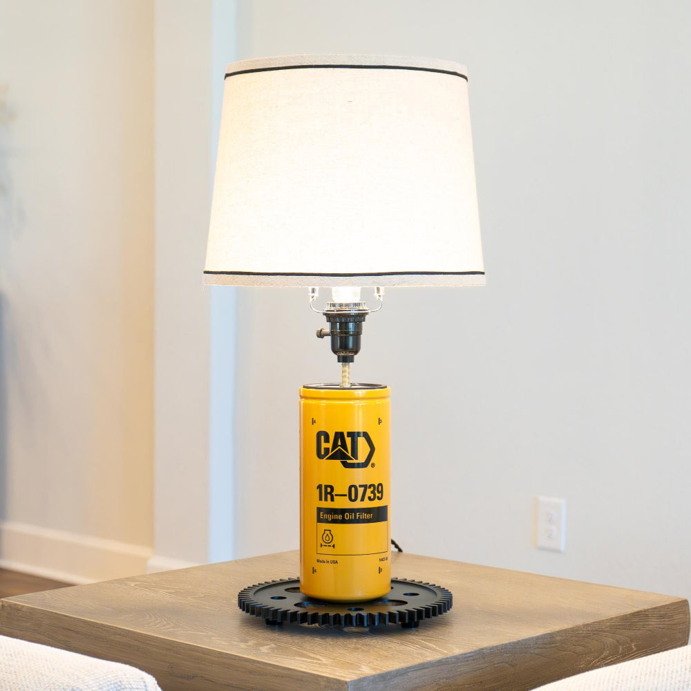 Yellow Caterpillar oil can repurposed as a lamp on a wooden surface.