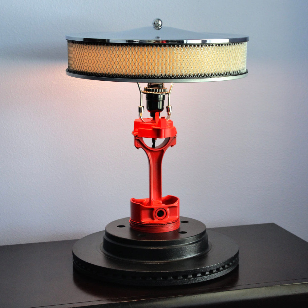 Table lamp with red metal base and black and white shade on a dark surface.