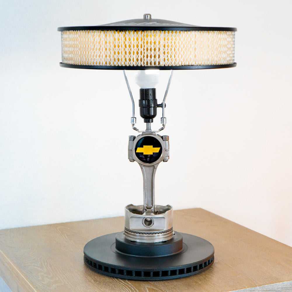 Lamp made from a car engine block with a Chevrolet logo on a wooden platform.