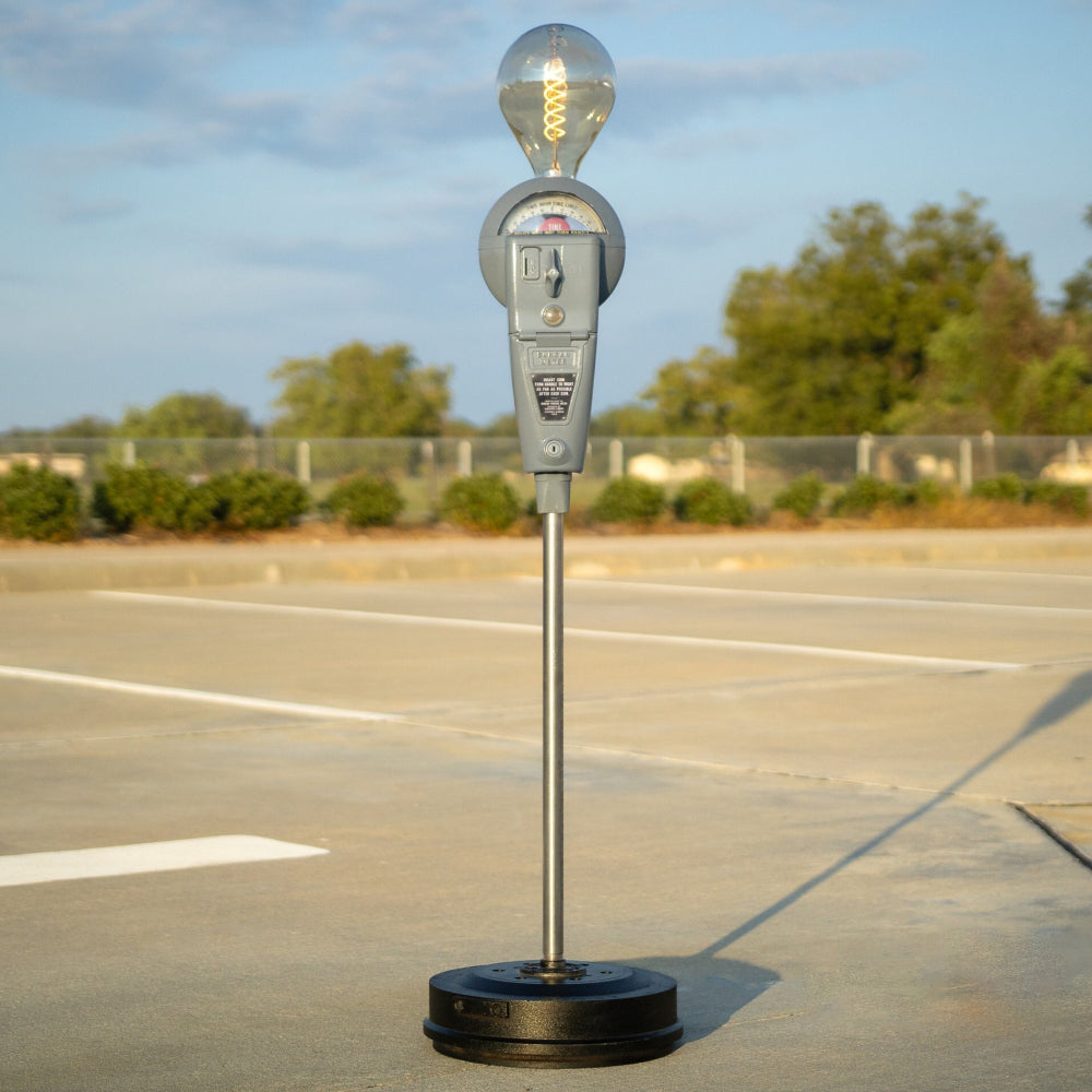 Decorative light bulb on a stand in an empty parking lot with trees in the background.