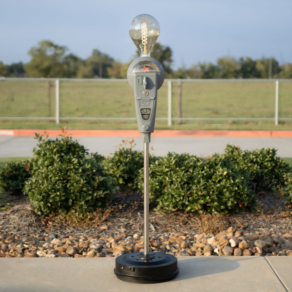 Vintage parking meter on a stand with a clear sky and greenery in the background
