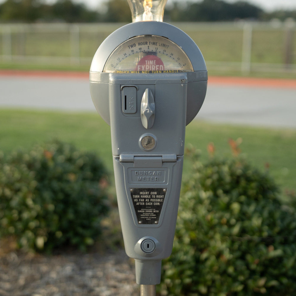 Vintage parking meter with a blurred background of grass and pavement