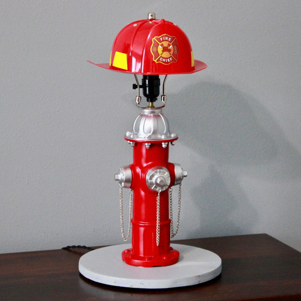 Red fire hydrant lamp with a fire helmet on top against a gray background