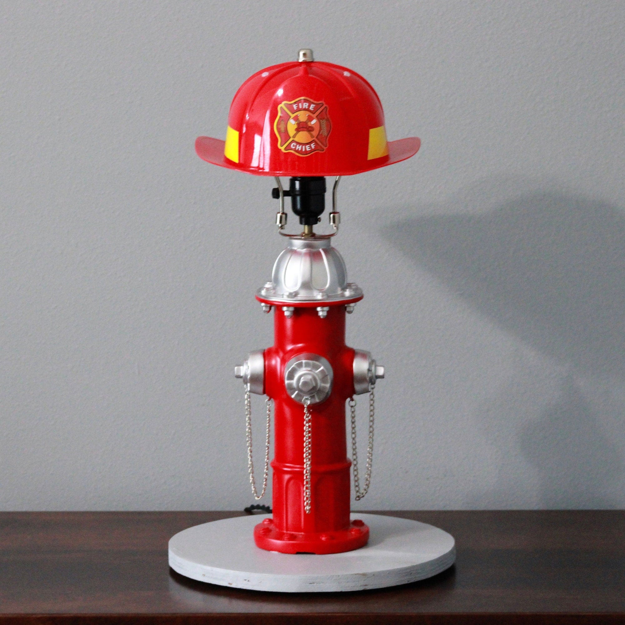 Red fire hydrant lamp with a fire helmet on top against a gray background