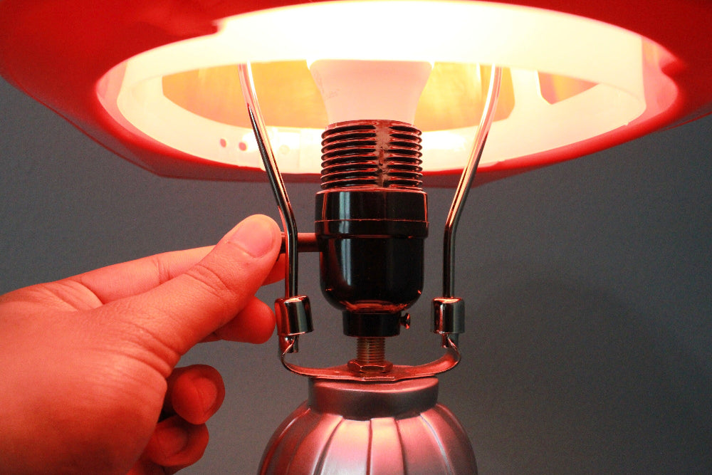 Hand holding a vintage-style lamp with a red shade against a dark background
