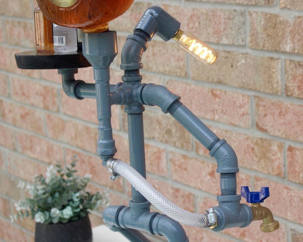 Decorative wall light fixture made from pipes and a bottle against a brick wall.
