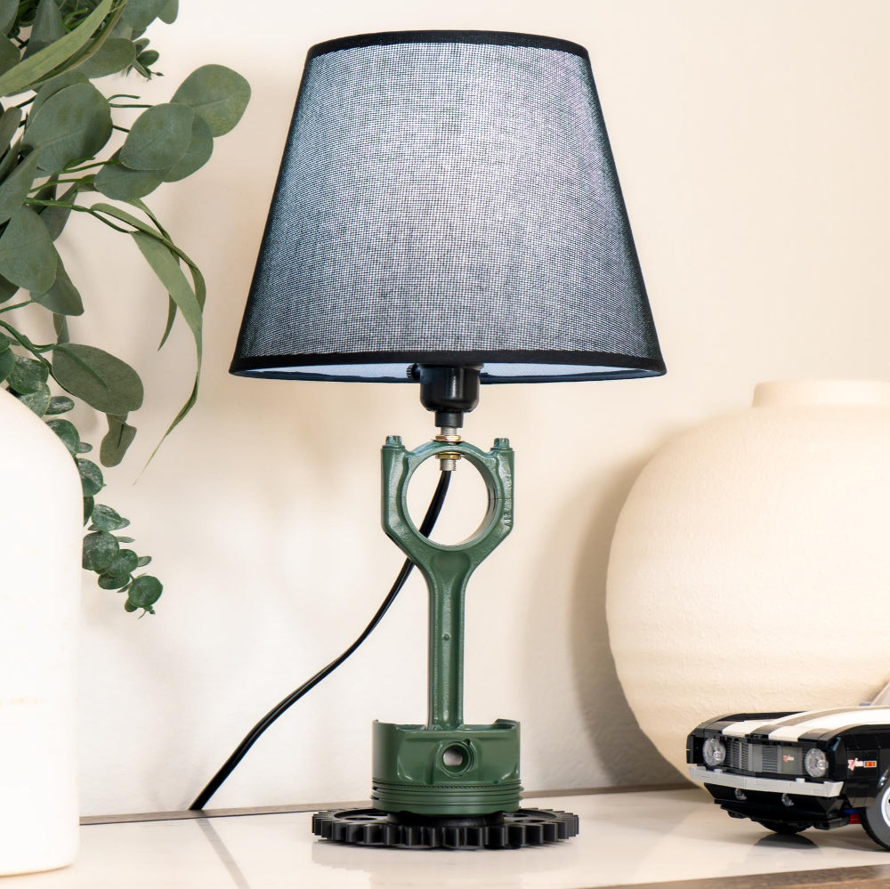 Table lamp with green base and black shade on a surface with decorative items.
