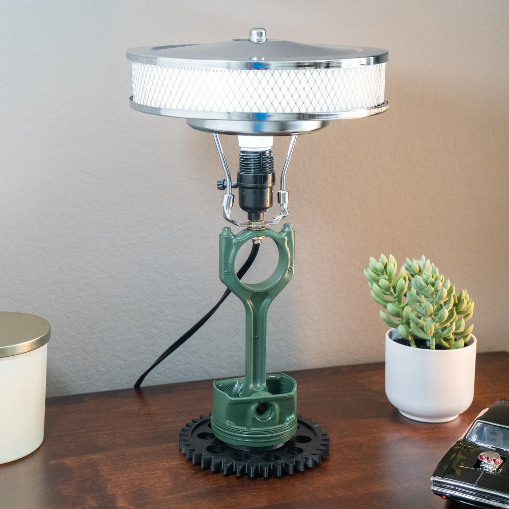 Table lamp with green base and silver top on a wooden surface with a candle and plant.