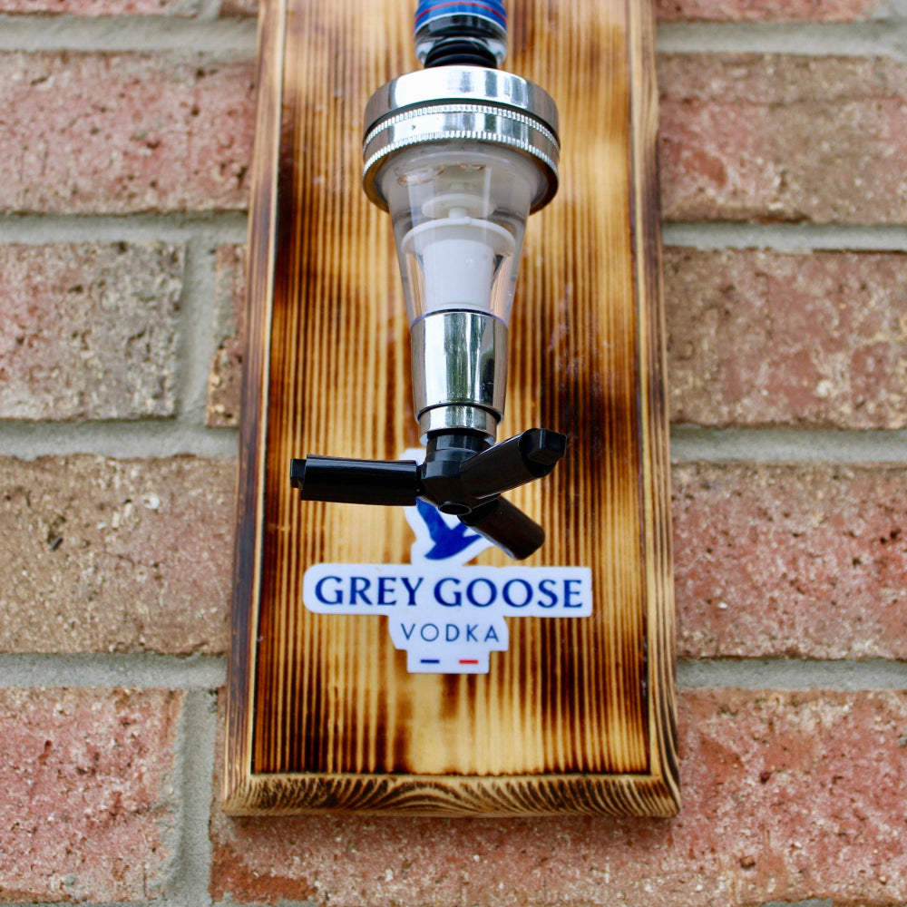 Wooden vodka dispenser with Grey Goose label against a brick wall