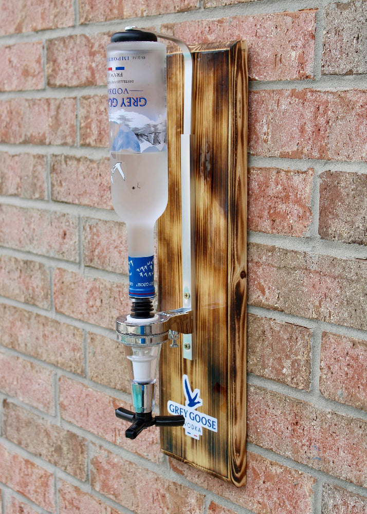 Wall-mounted bottle filler with a bottle of Grey Goose vodka against a brick wall.