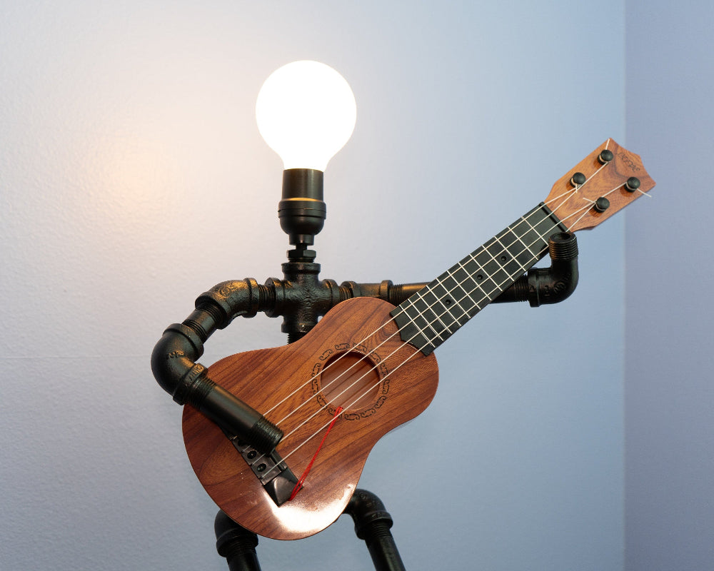 Ukulele modified with black pipes and a light bulb on a gray background