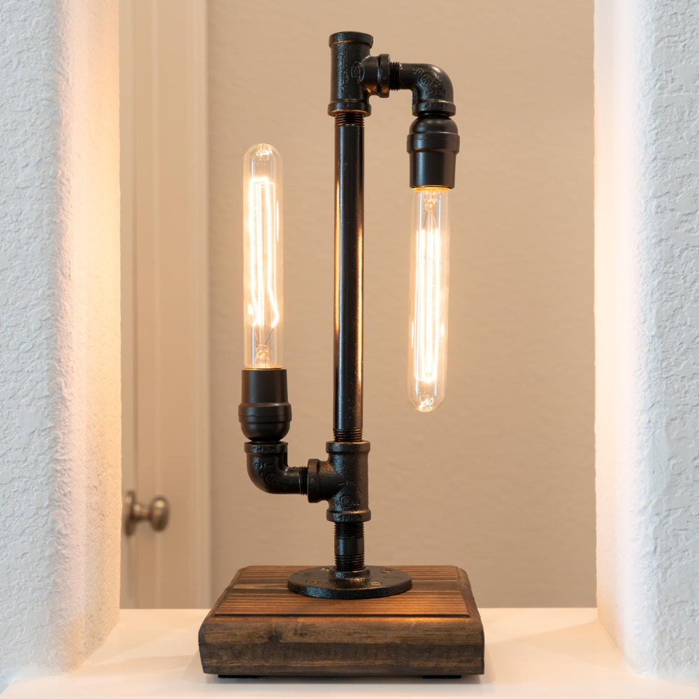 Industrial-style table lamp with black pipes and wooden base on a white surface.