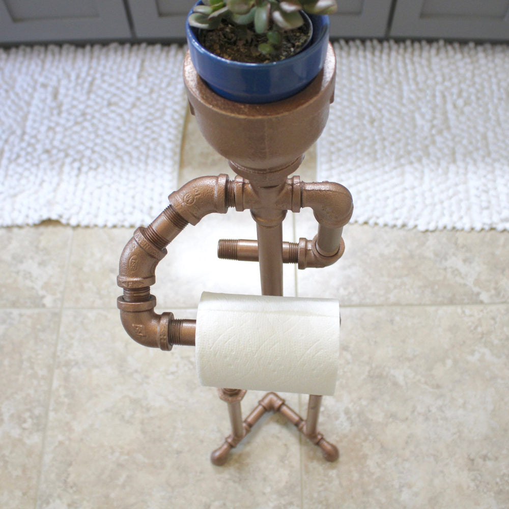 Pipe-themed toilet paper holder with a plant on a white rug.