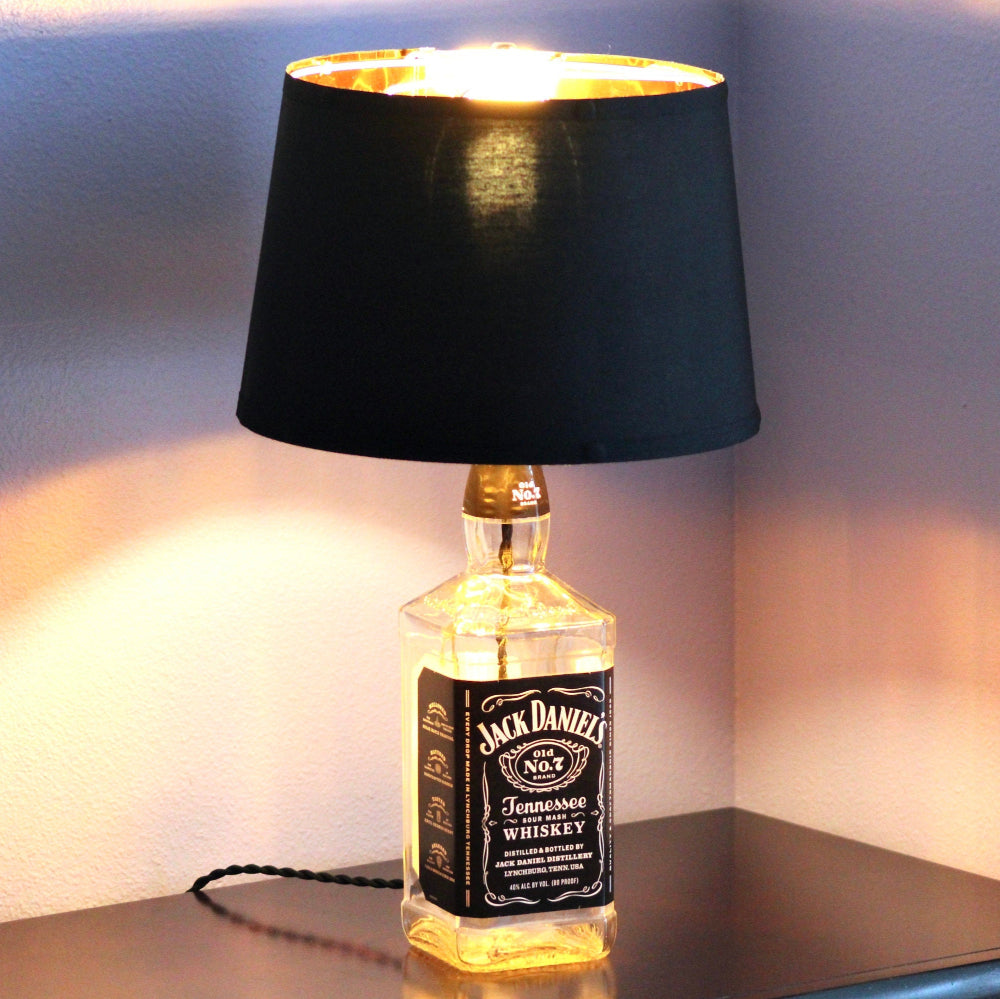 Jack Daniel's whiskey bottle lamp with a black shade on a table.