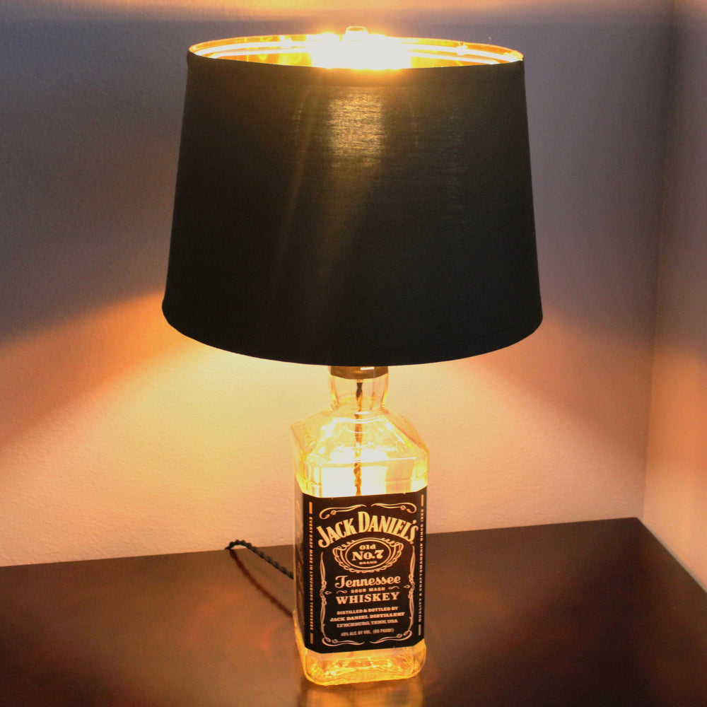 Jack Daniel's whiskey bottle lamp with a black shade on a surface.