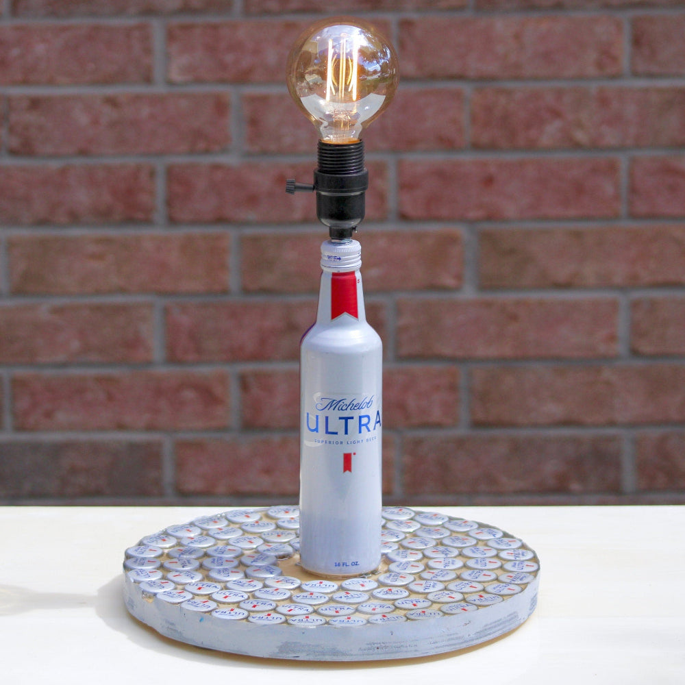 Lamp made from a Michelob Ultra beer bottle on a textured base against a brick wall.