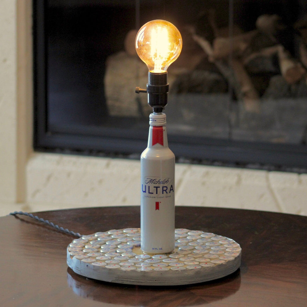 Bottle ofultra on a stand with a light bulb, placed on a table in front of a fireplace.