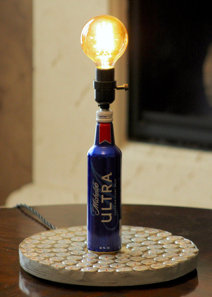 Bottle lamp made from a Michelob Ultra beer bottle with a light bulb on a wooden surface.
