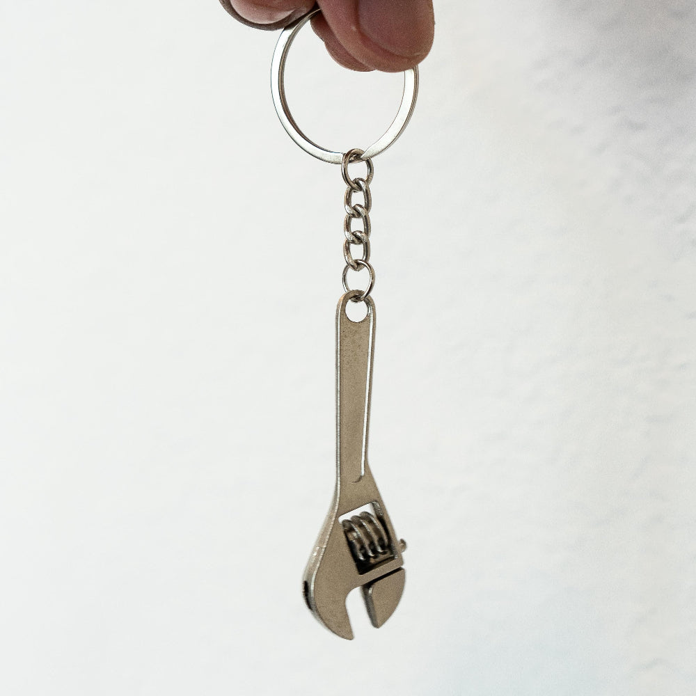 Metal wrench keychain held by a hand against a white background