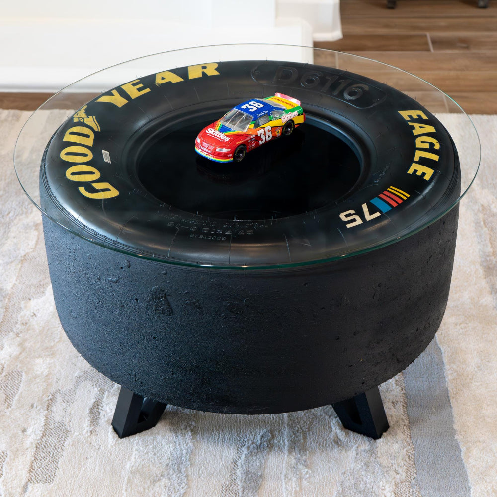 Black Goodyear tire-shaped coffee table with a toy car on top in a room setting.