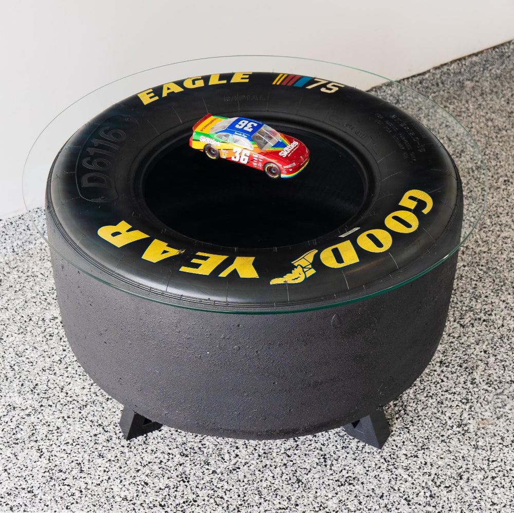 Black tire-shaped stool with 'Good Year' branding on a gray floor.