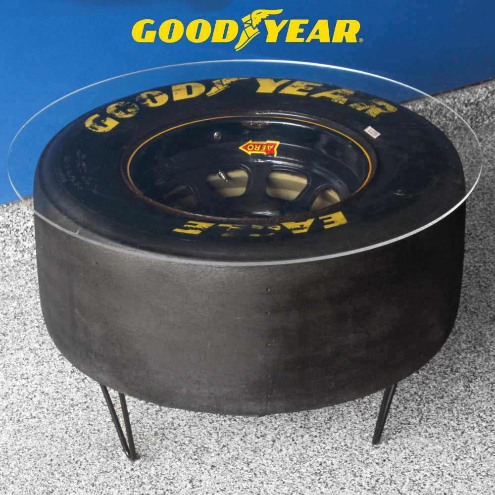 Fire pit made from a Goodyear tire with glass top on a gravel surface.