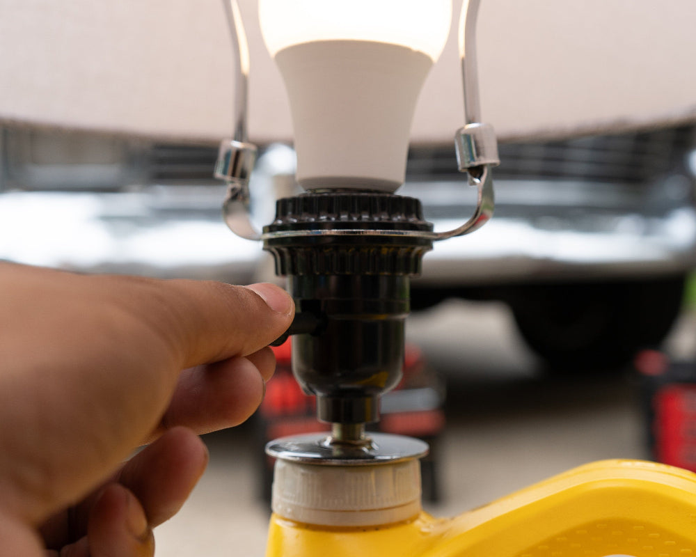 Hand adjusting a light bulb in a yellow lantern with a blurred vehicle in the background