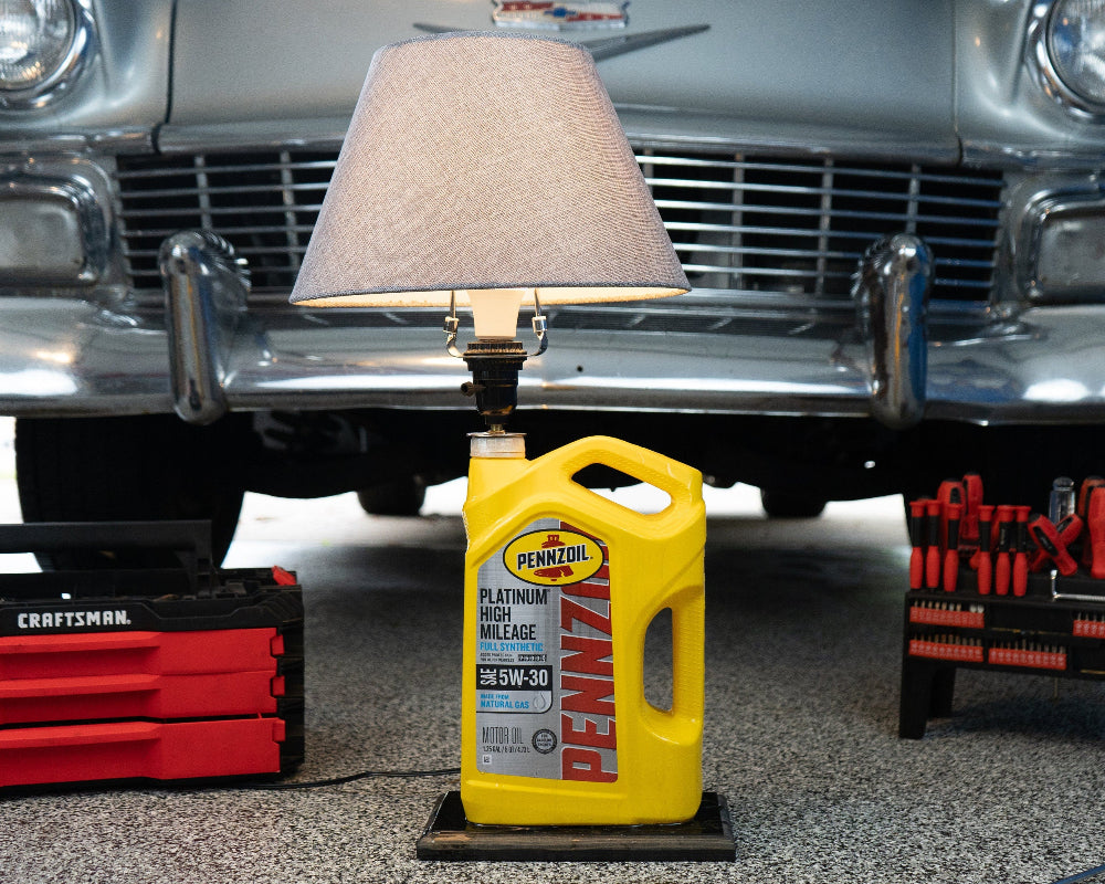 Yellow Pennzoil bottle with a lamp on a car bumper, surrounded by tools and equipment.