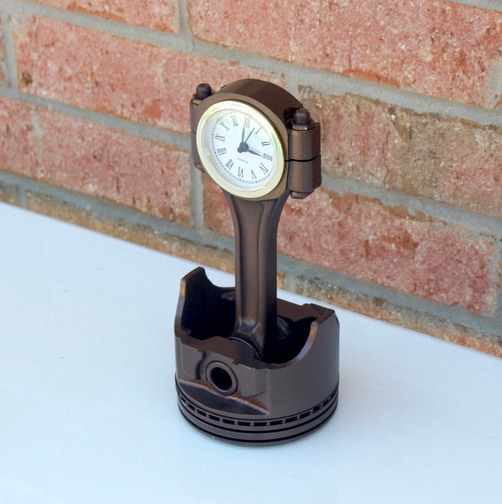Piston-shaped clock on a white surface with a brick wall background