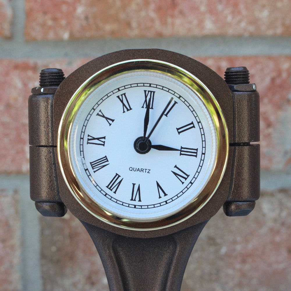 Bronze wristwatch with a white face and black Roman numerals against a brick wall background