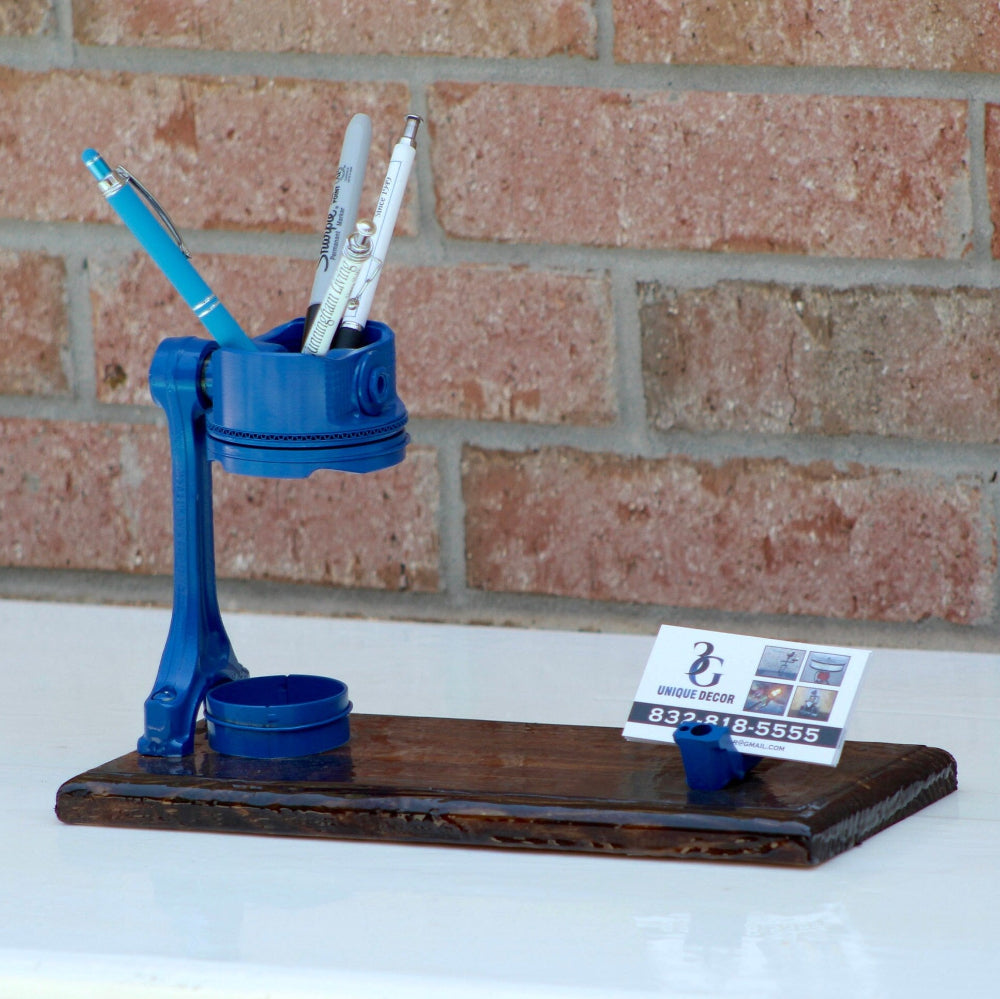 Blue pen holder with pens and a business card on a white surface with a brick wall background