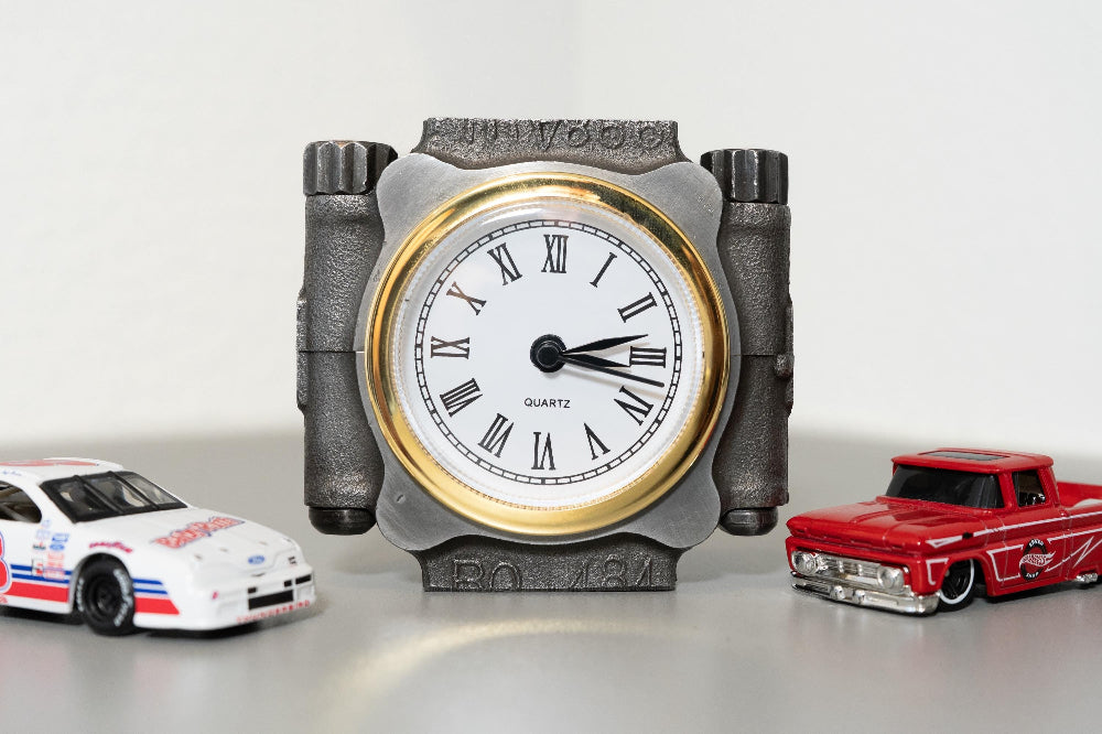 Decorative clock with Roman numerals on a white background, flanked by toy cars.