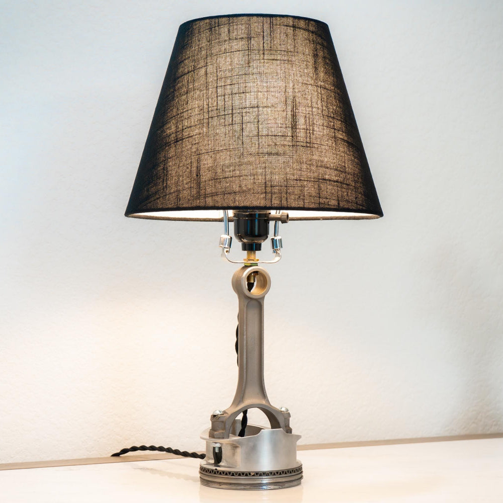 Table lamp with black shade on a white surface, with a plant in the background