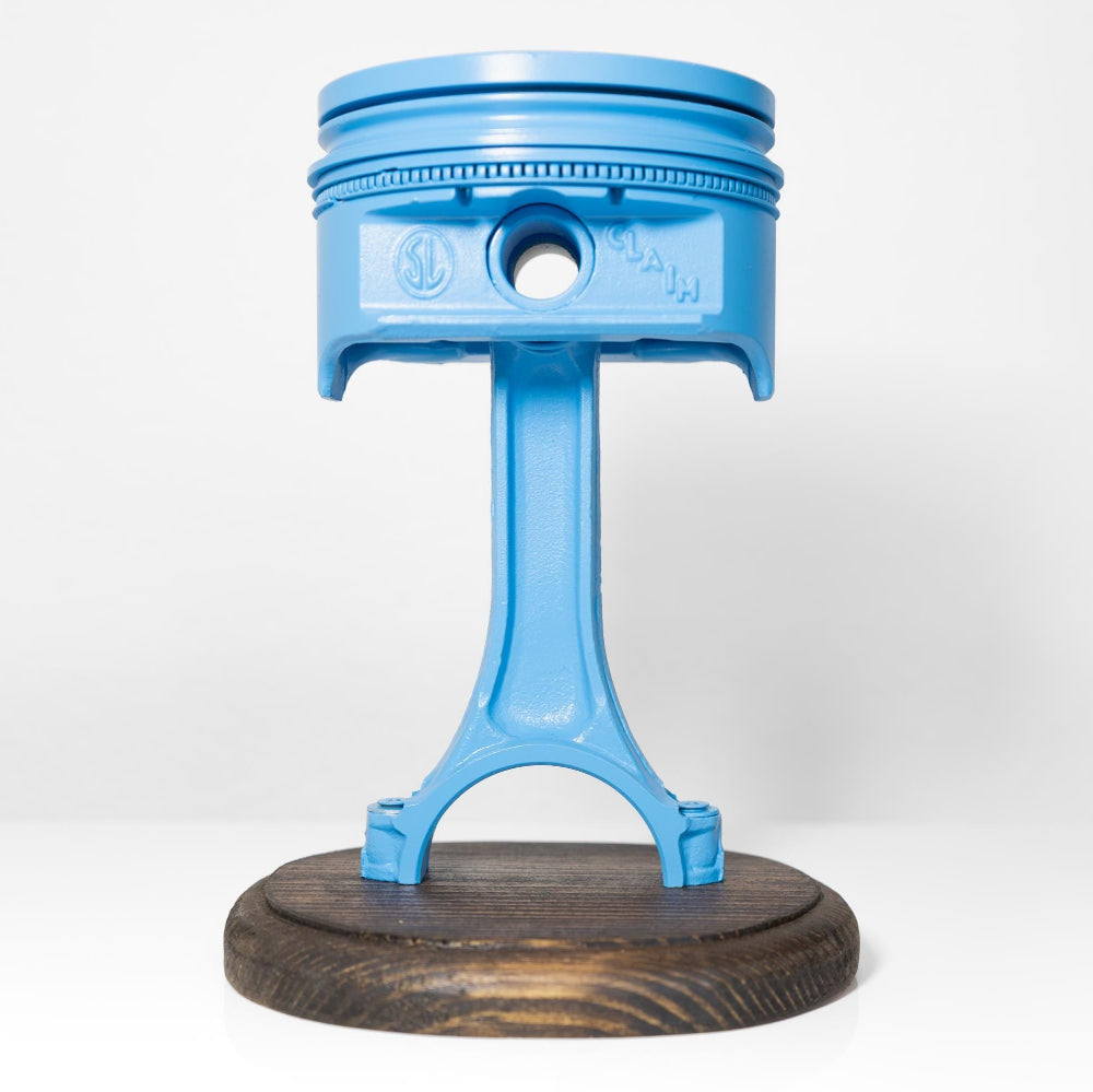 Blue metal piston on a wooden base against a white background
