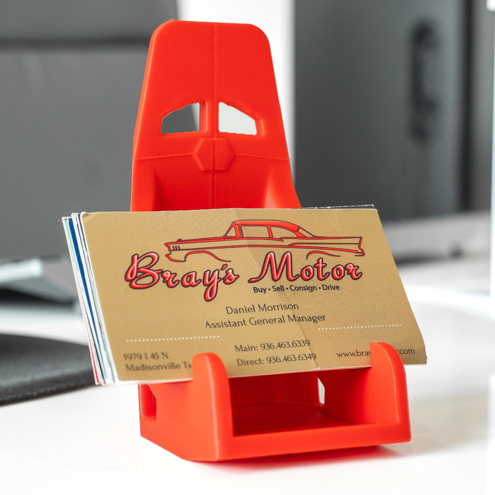 Red business card holder with a business card displaying 'Bray's Motor' on a desk.