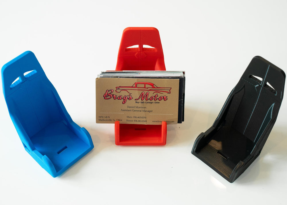 Three car seat models in blue, red, and black with a business card holder in the center.