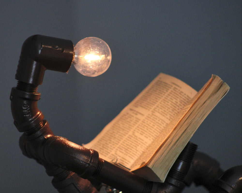 Light bulb on a book held by black metal pipes against a dark background
