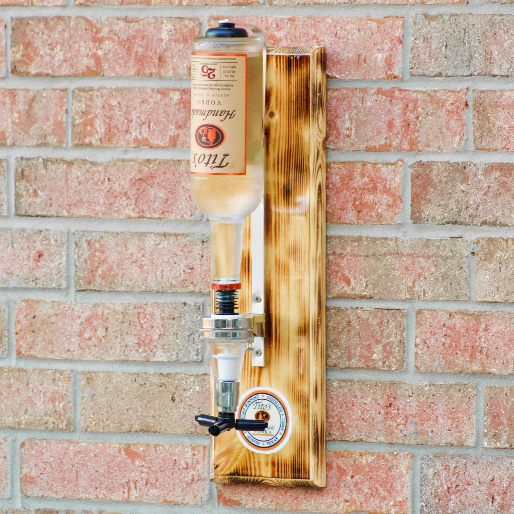 Bottle of Tito's vodka mounted on a wooden holder against a brick wall.