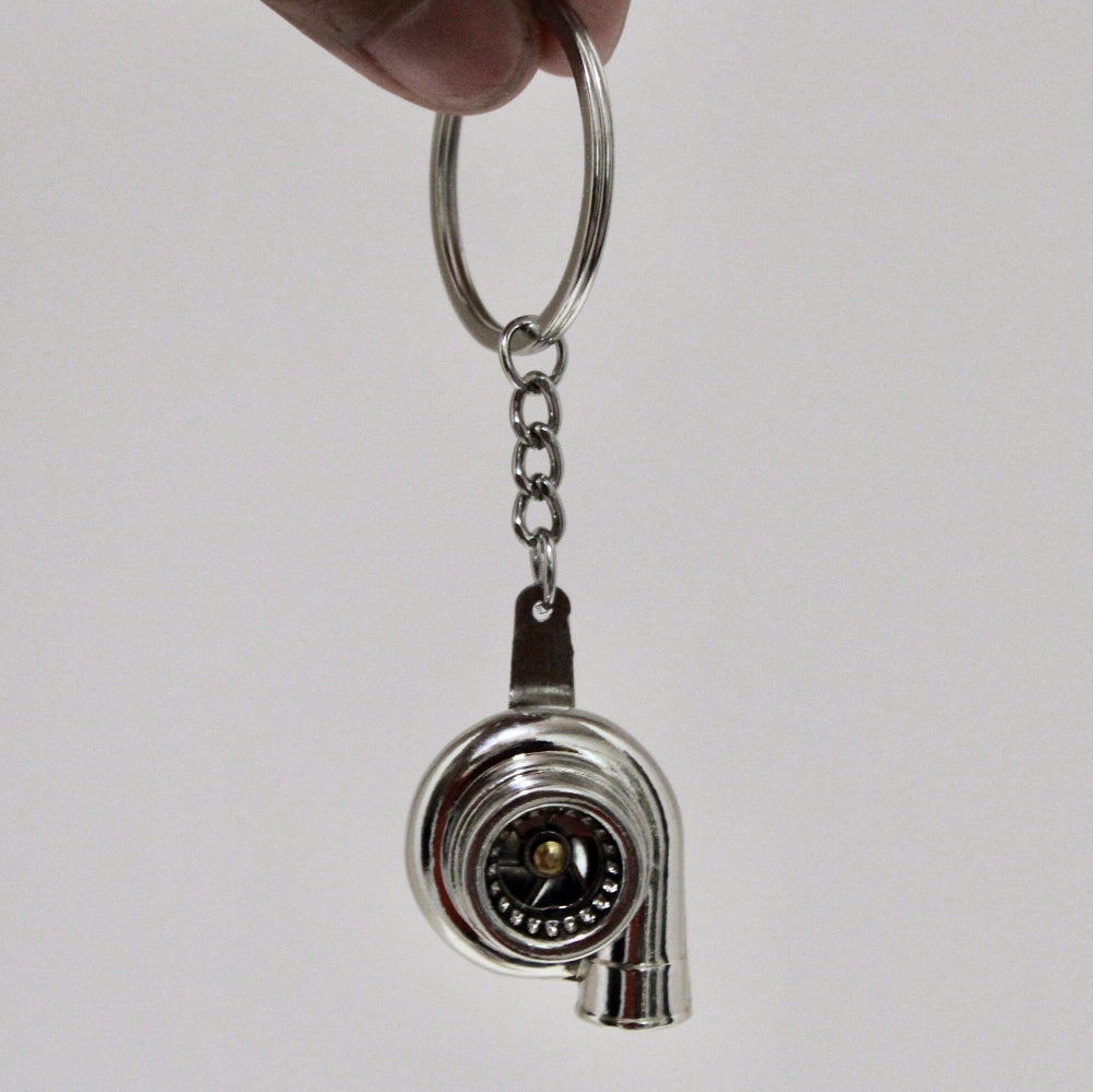 Metal keychain shaped like a turbocharger on a plain background