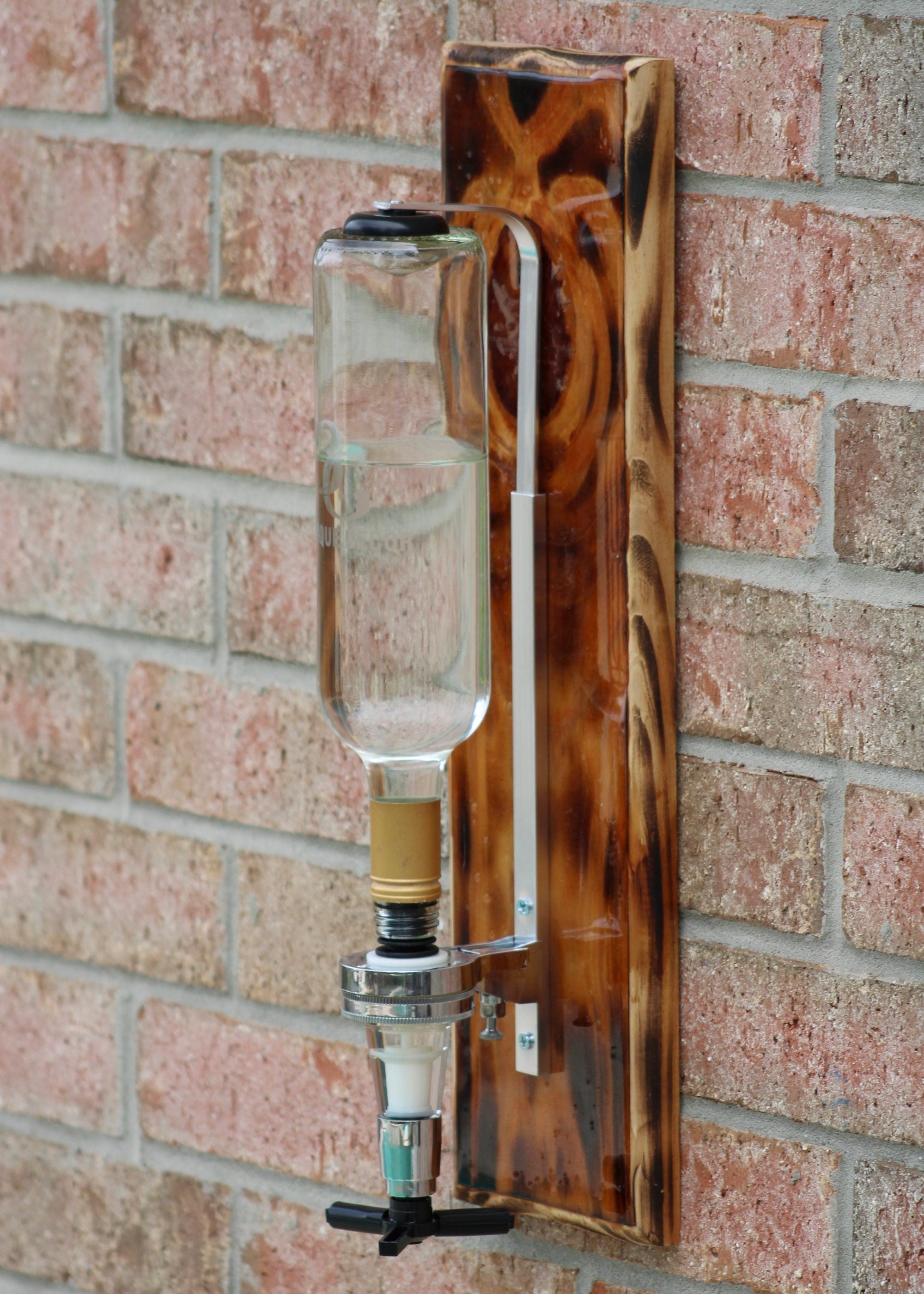 Wooden wall-mounted bottle holder with a clear bottle against a brick wall.