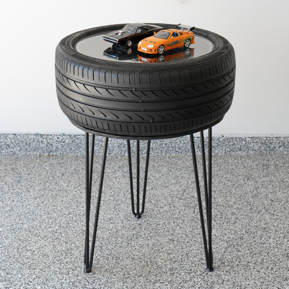 Table made from a tire with model cars on top, set against a white wall.