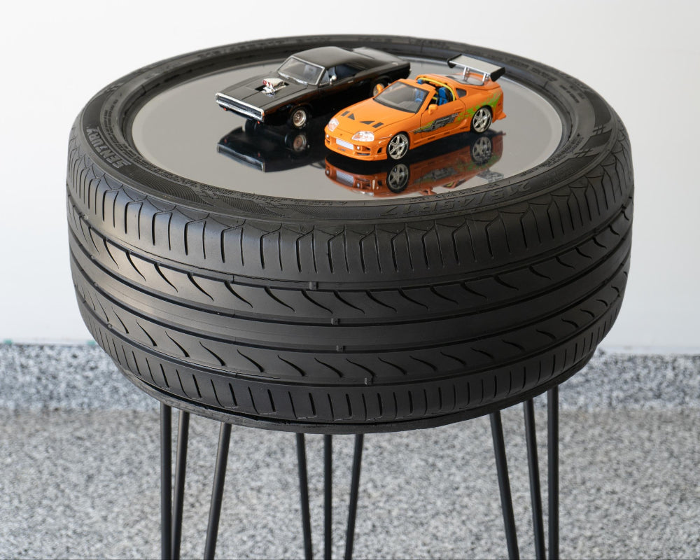 Table made from stacked car tires with a reflective surface and toy cars on top.