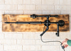 Wall-mounted industrial-style light fixture with wooden panel and black pipes on a white brick wall.
