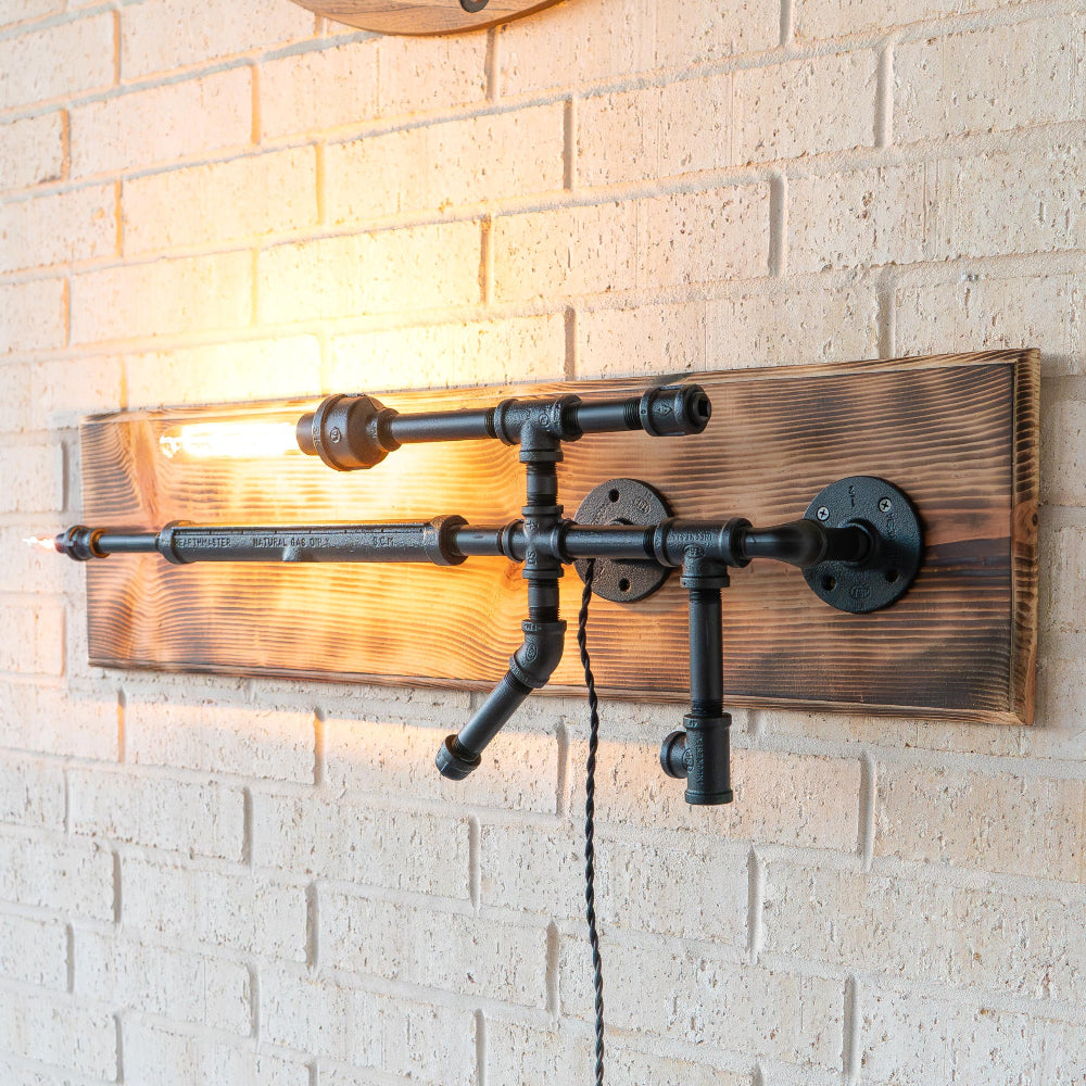Wall-mounted industrial-style light fixture with wooden panel and metal pipes on a brick wall.